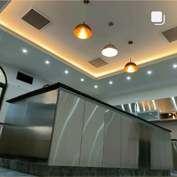 Modern kitchen with a sleek stainless steel counter, stylish pendant lights, and elegant ceiling design featuring LED lighting.