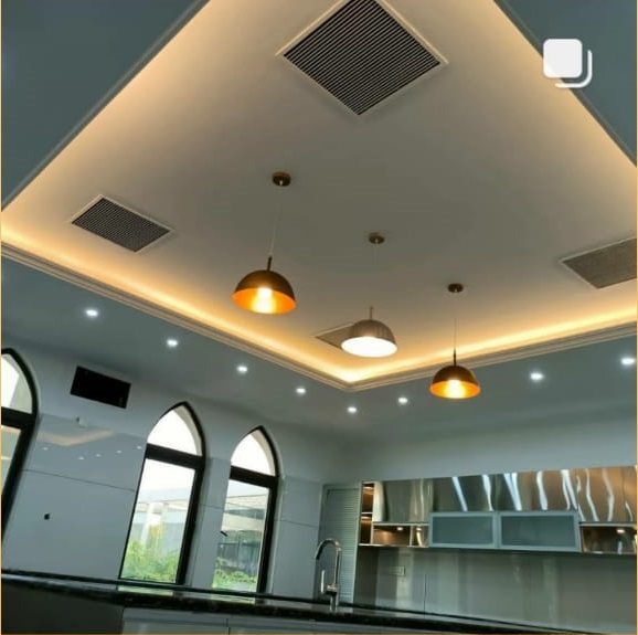 A modern kitchen with elegant ceiling lights, recessed lighting, air vents, and large windows, creating a bright and inviting atmosphere.