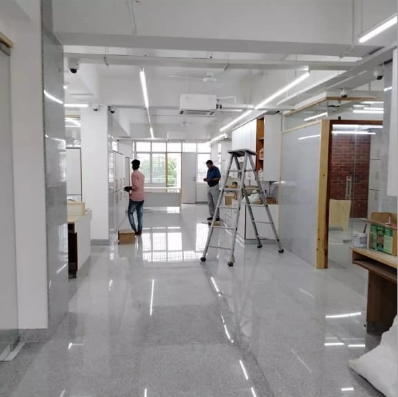 Two men are working in a bright, modern room with polished floors, a ladder, and construction materials, preparing for an installation.