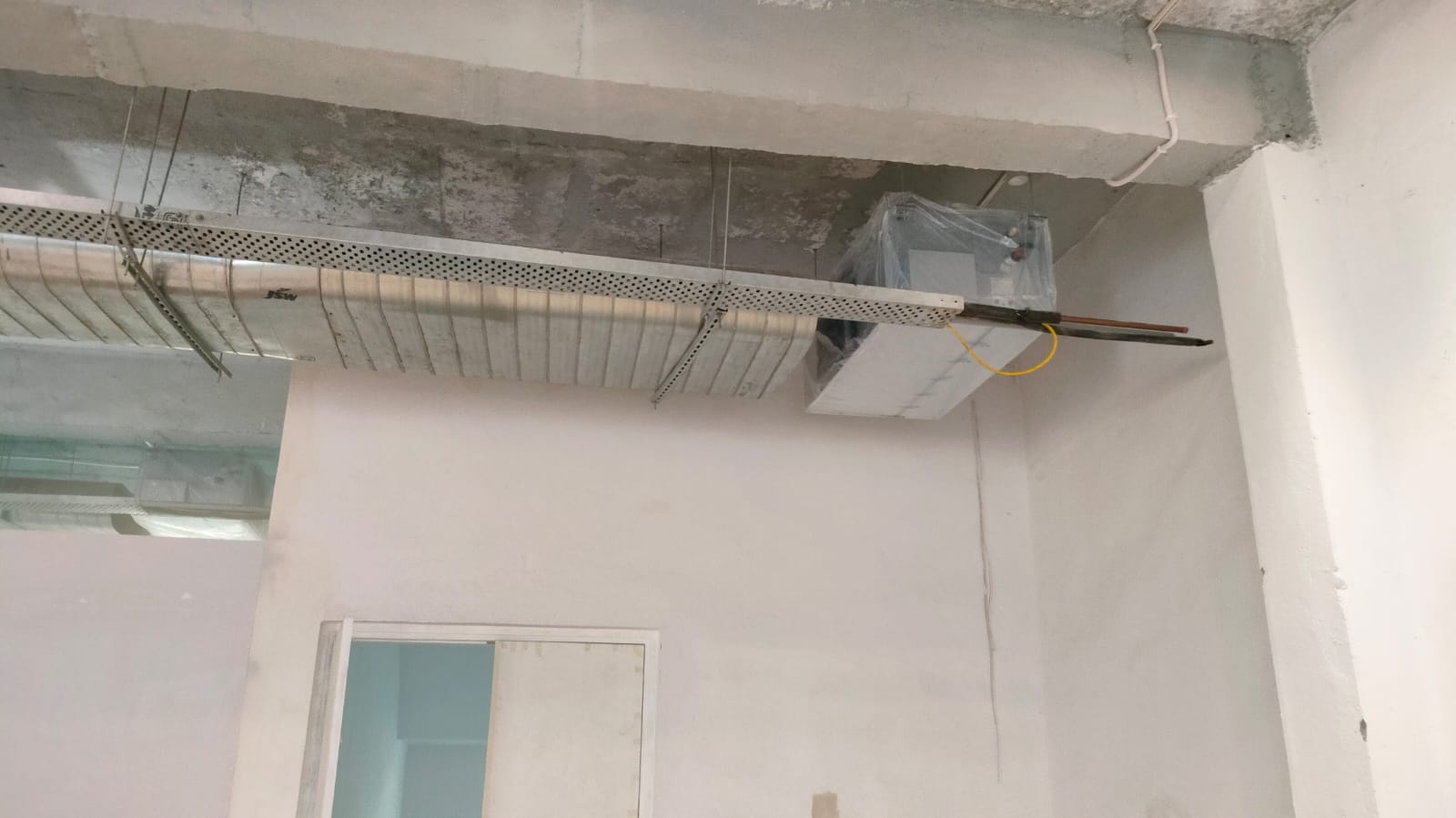 A ceiling with exposed ventilation ducting and an air conditioning unit, in a minimally decorated, unfinished room.