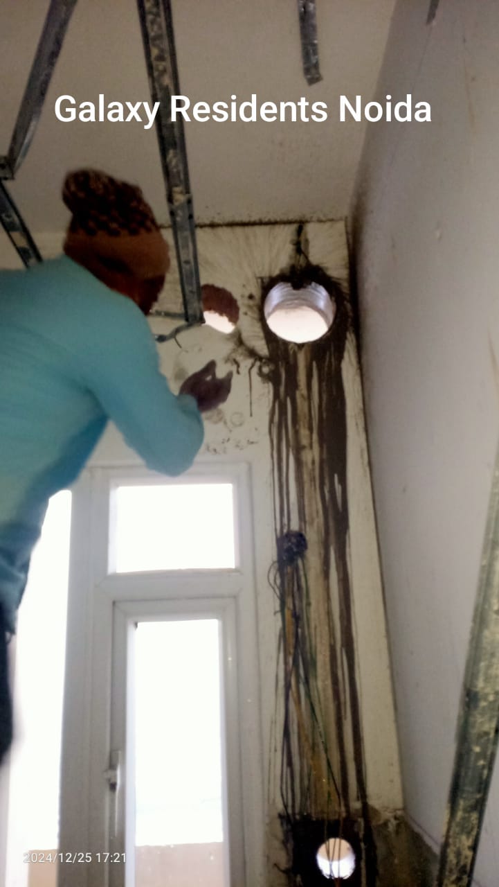 A worker repairs wall holes, with tools and electrical wires visible, in a room at Galaxy Residents, Noida.